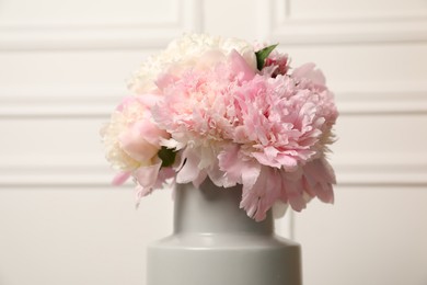 Photo of Beautiful peonies in vase near white wall, closeup