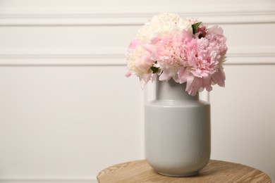 Photo of Beautiful peonies in vase on wooden table near white wall. Space for text