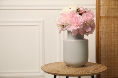 Photo of Beautiful peonies in vase on wooden table indoors. Space for text