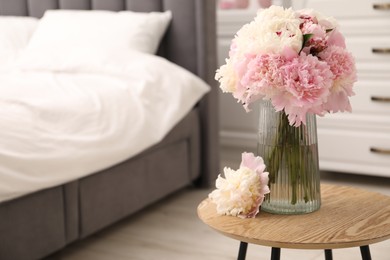 Photo of Beautiful peonies in vase on wooden table indoors. Space for text