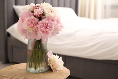 Photo of Beautiful peonies in vase on wooden table indoors. Space for text