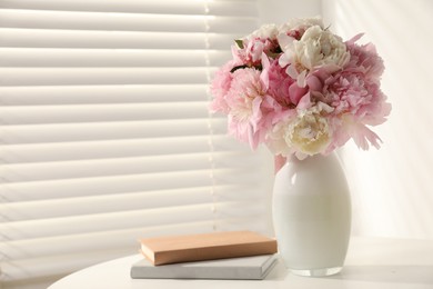 Photo of Bouquet of beautiful peonies in vase and books on white table indoors. Space for text