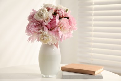 Photo of Bouquet of beautiful peonies in vase and books on white table indoors. Space for text