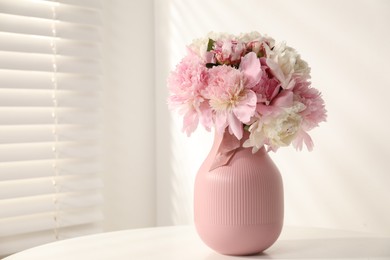 Photo of Bouquet of beautiful peonies in vase on white table indoors. Space for text