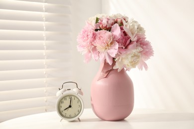 Photo of Bouquet of beautiful peonies and alarm clock on white table indoors