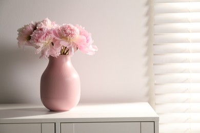 Photo of Beautiful peonies in vase on white dresser indoors. Space for text