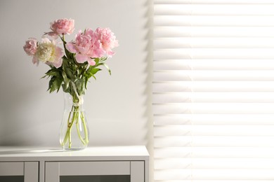 Photo of Beautiful peonies in vase on white dresser indoors. Space for text