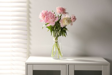 Photo of Beautiful peonies in vase on white dresser indoors