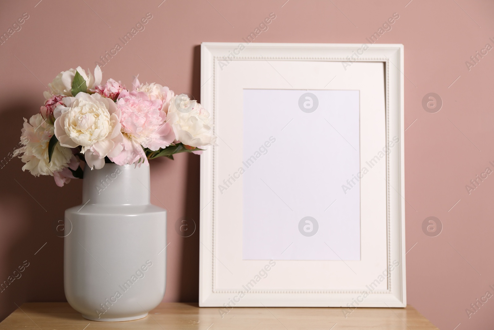 Beautiful peonies in vase and picture frame on wooden dresser near pink wall. Space for text Photo of Beautiful peonies in vase and picture frame on wooden dresser near pink wall. Space for text