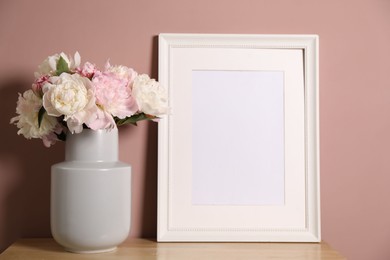 Photo of Beautiful peonies in vase and picture frame on wooden dresser near pink wall. Space for text