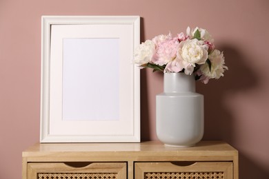 Photo of Beautiful peonies in vase and picture frame on wooden dresser near pink wall. Space for text