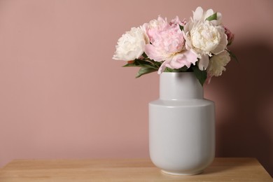 Photo of Beautiful peonies in vase on wooden dresser near pink wall. Space for text