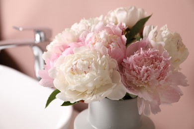 Photo of Beautiful peonies in vase and sink on table near pink wall, closeup