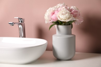 Photo of Beautiful peonies in vase and sink on white table near pink wall