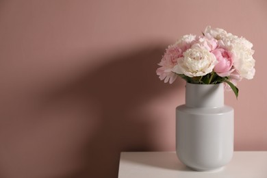 Photo of Beautiful peonies in vase on white table near pink wall. Space for text