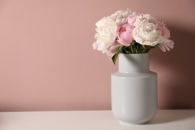 Photo of Beautiful peonies in vase on white table near pink wall. Space for text