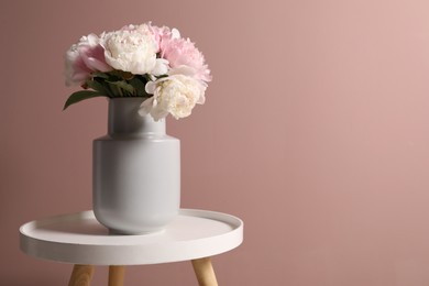 Photo of Beautiful peonies in vase on white table near pink wall. Space for text