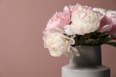 Photo of Beautiful peonies in vase near pink wall, closeup. Space for text