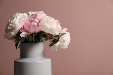 Photo of Beautiful peonies in vase near pink wall, closeup. Space for text
