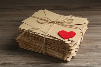 Photo of Stack of love letters and paper heart on wooden table, closeup