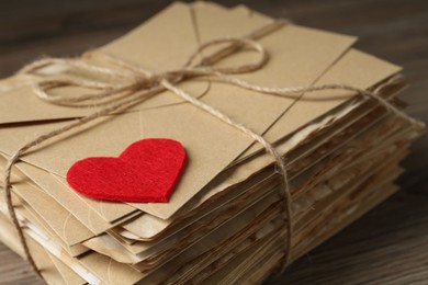 Photo of Stack of love letters and paper heart on wooden table, closeup