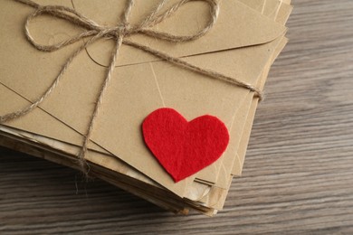 Photo of Stack of love letters and paper heart on wooden table, top view