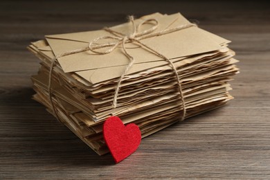 Photo of Stack of love letters and paper heart on wooden table, closeup