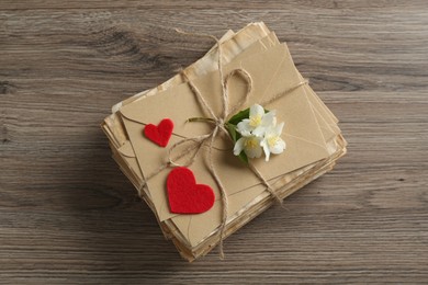 Photo of Stack of love letters, paper hearts and flowers on wooden table, top view