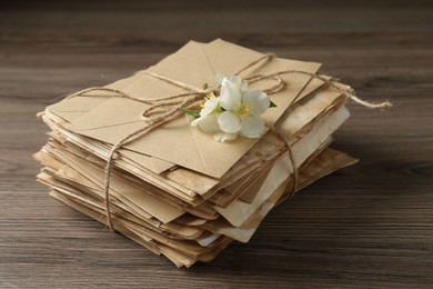 Photo of Stack of love letters and flowers on wooden table, closeup
