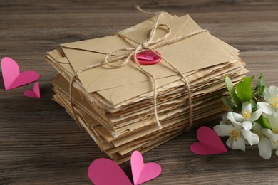 Photo of Stack of love letters, paper hearts and flowers on wooden table, closeup