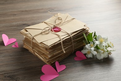 Photo of Stack of love letters, paper hearts and flowers on wooden table, closeup