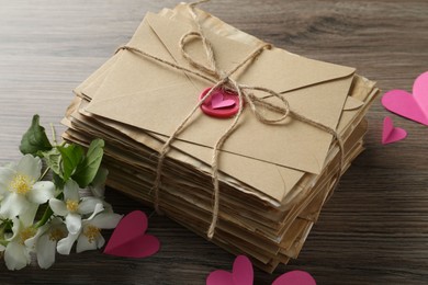 Photo of Stack of love letters, paper hearts and flowers on wooden table, closeup