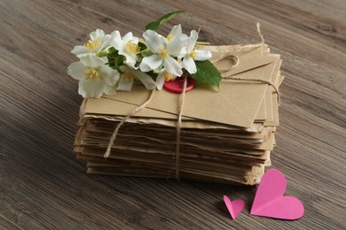 Photo of Stack of love letters, paper hearts and flowers on wooden table, closeup
