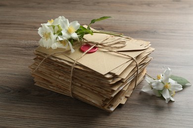 Photo of Stack of love letters and flowers on wooden table, closeup