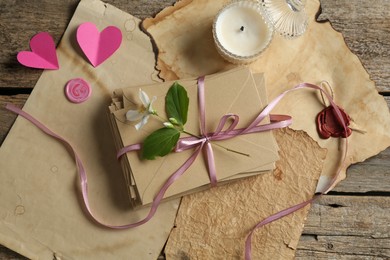 Photo of Stack of love letters, flower, paper hearts, candle and parchment sheets on wooden table, flat lay