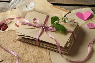 Photo of Stack of love letters, flower, paper hearts, candle and parchment sheets on wooden table, closeup