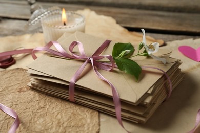 Photo of Stack of love letters, flower, candle and parchment sheets on wooden table, closeup