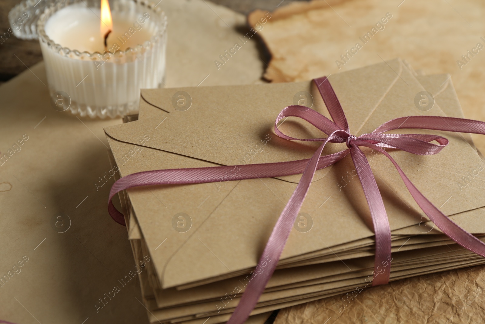 Stack of love letters, candle and parchment sheets on wooden table, closeup Photo of Stack of love letters, candle and parchment sheets on wooden table, closeup