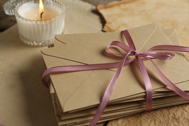 Photo of Stack of love letters, candle and parchment sheets on wooden table, closeup