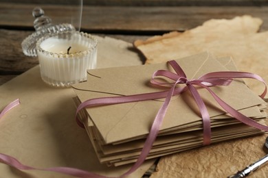 Photo of Stack of love letters, candle and parchment sheets on wooden table, closeup