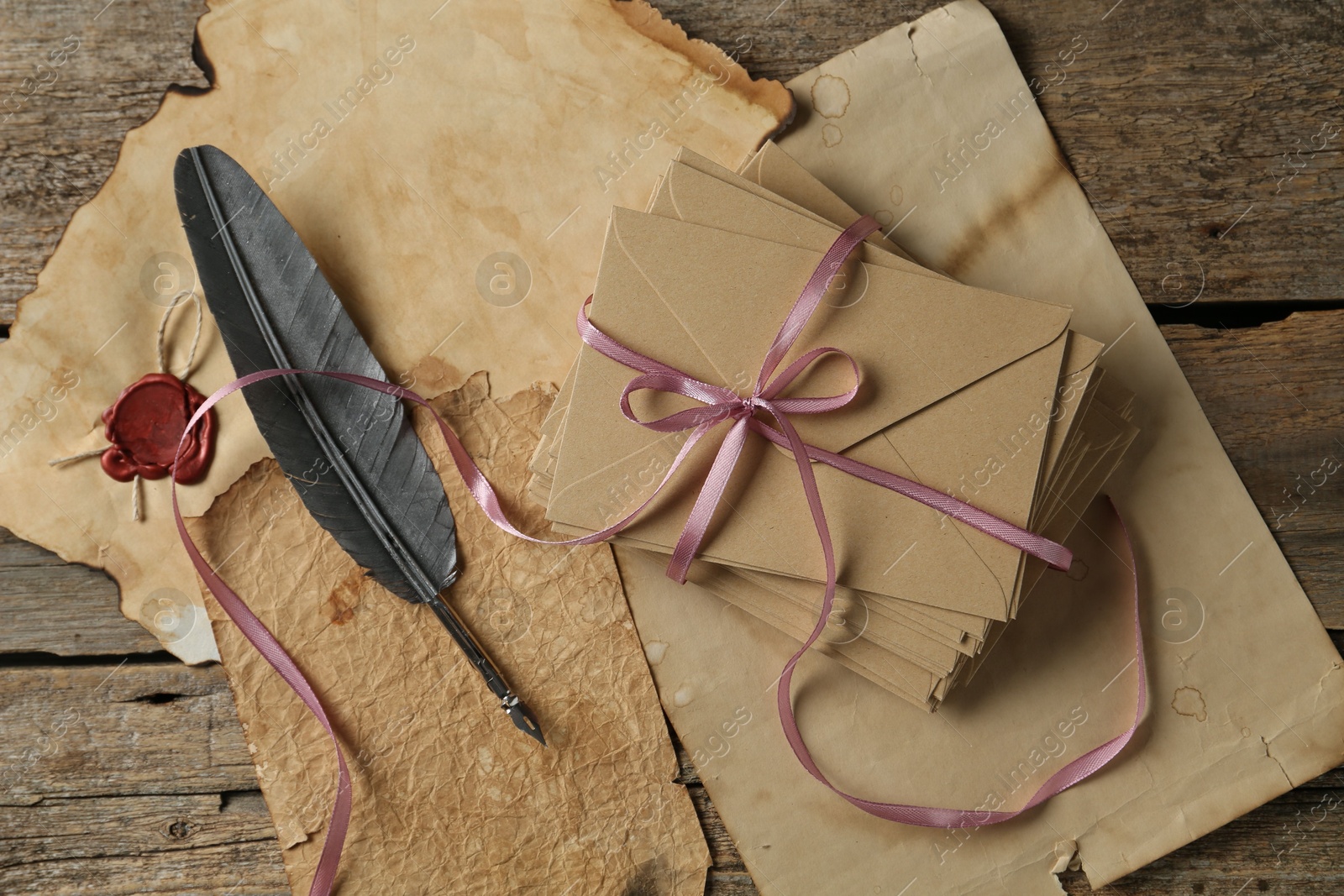 Stack of love letters, quill and parchment sheets on wooden table, flat lay Photo of Stack of love letters, quill and parchment sheets on wooden table, flat lay