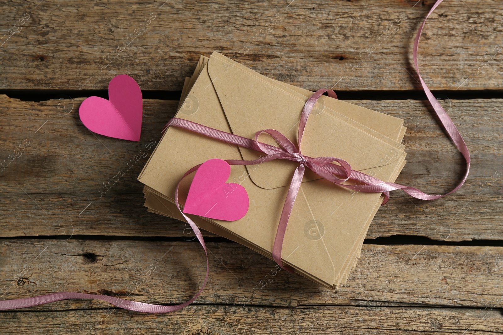 Photo of Stack of love letters and paper hearts on wooden table, top view
