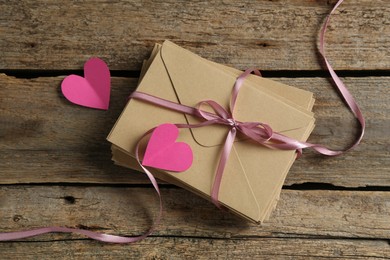Photo of Stack of love letters and paper hearts on wooden table, top view