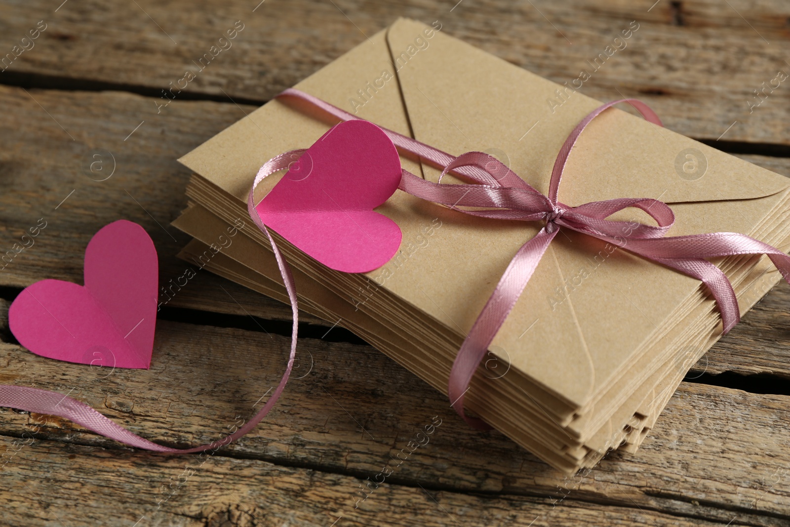 Photo of Stack of love letters and paper hearts on wooden table, closeup