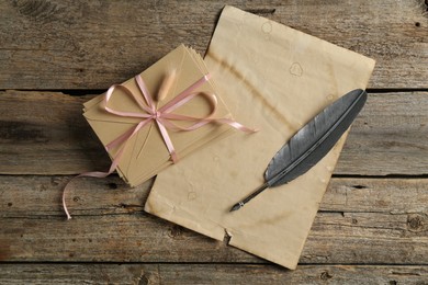 Photo of Stack of love letters, quill and parchment sheet on wooden table, top view