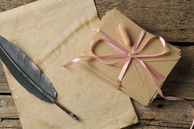 Photo of Stack of love letters, quill and parchment sheet on wooden table, top view