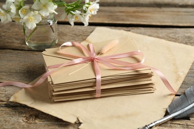 Photo of Stack of love letters, quill, parchment sheet and flowers on wooden table, closeup
