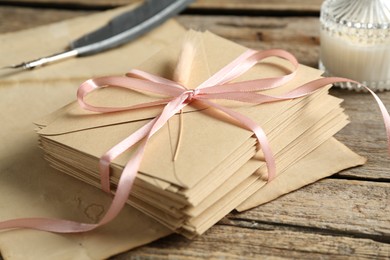 Photo of Stack of love letters, quill and parchment sheet on wooden table, closeup