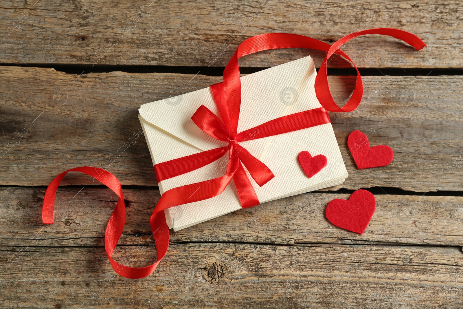 Photo of Stack of love letters and paper hearts on wooden table, top view