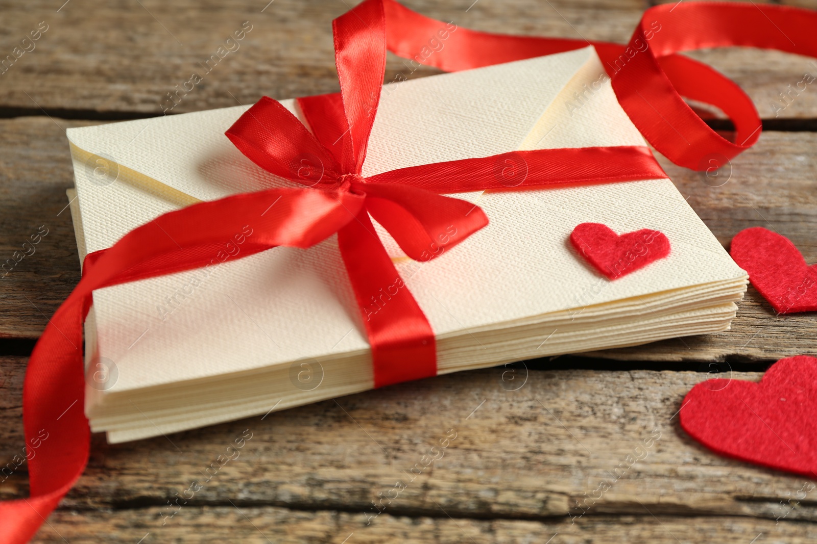 Photo of Stack of love letters and paper hearts on wooden table, closeup